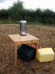 A tea urn on a table in a field, powered by a   generator underneath